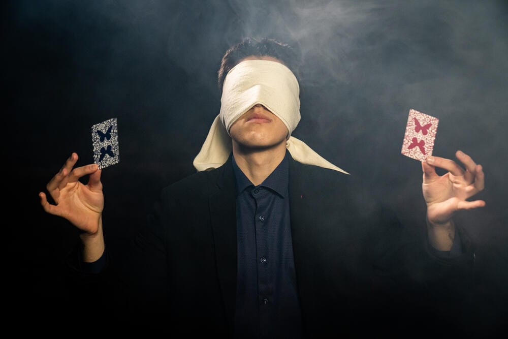 Rado Sheytanoff blindfolded, holding two playing cards in the smoke